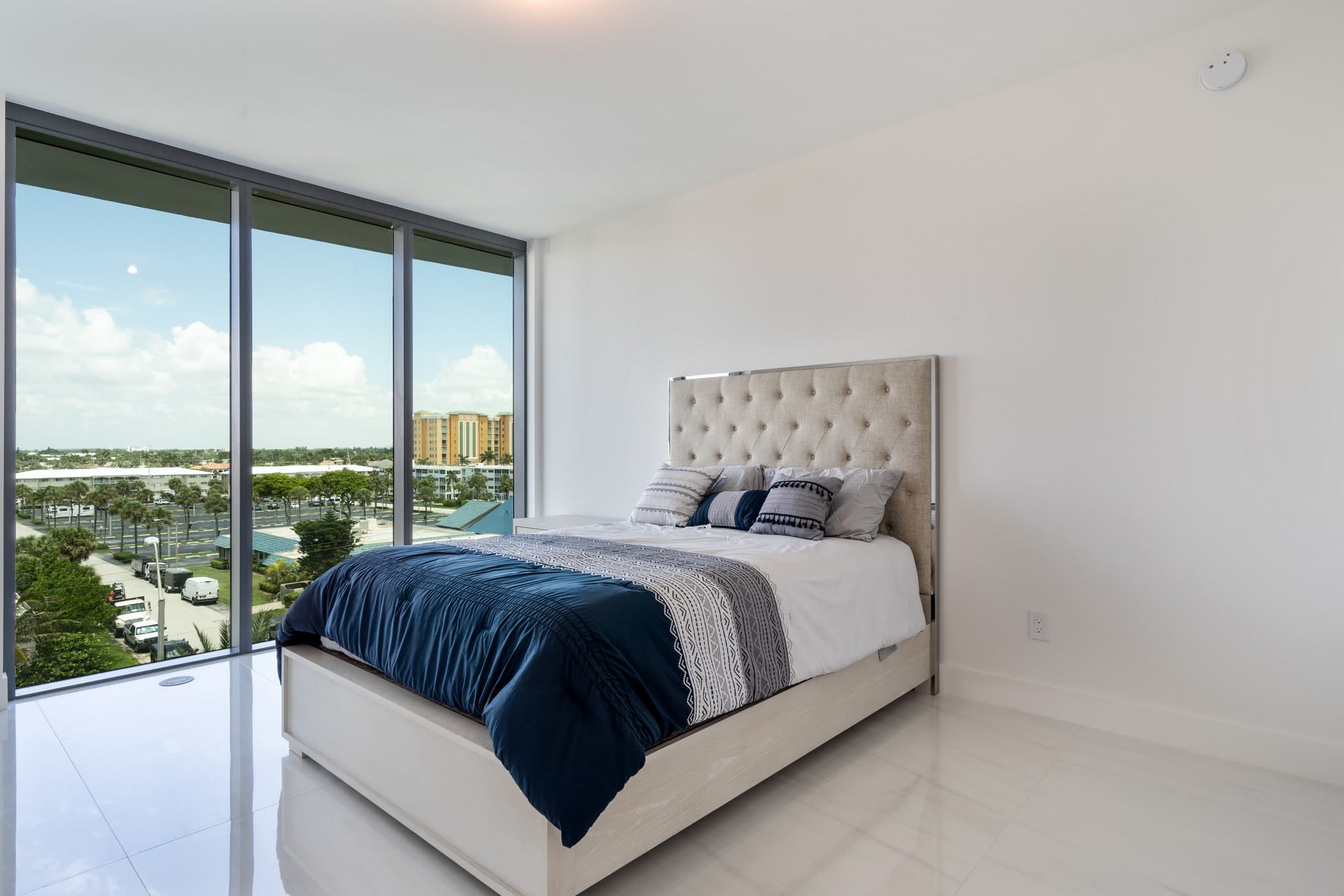 Bedroom with a tufted bed, white walls and floor-to-ceiling windows