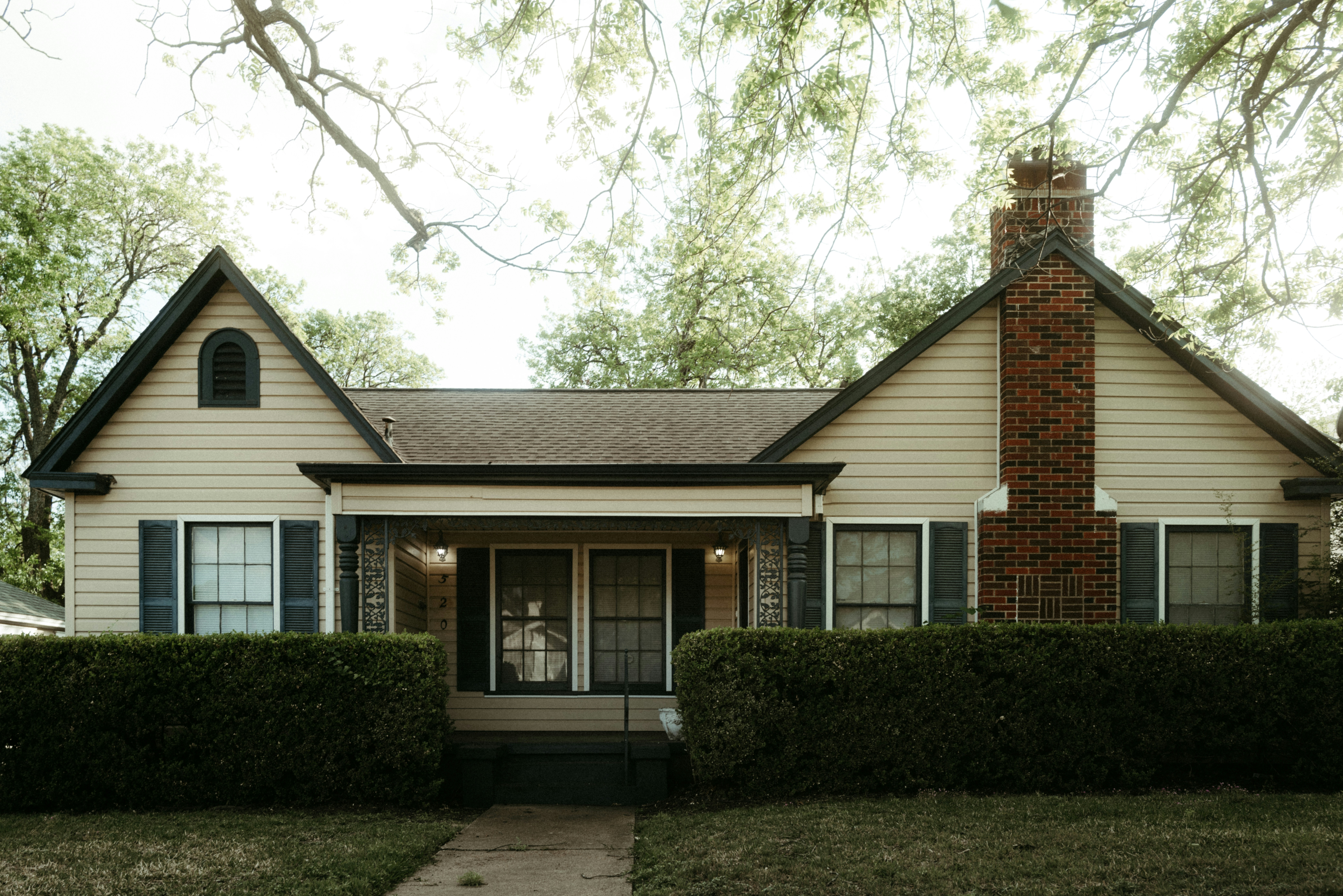 Outdated house facade with old siding and overgrown hedges